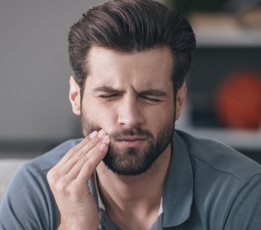 Man in need of restorative dentistry holding his cheek